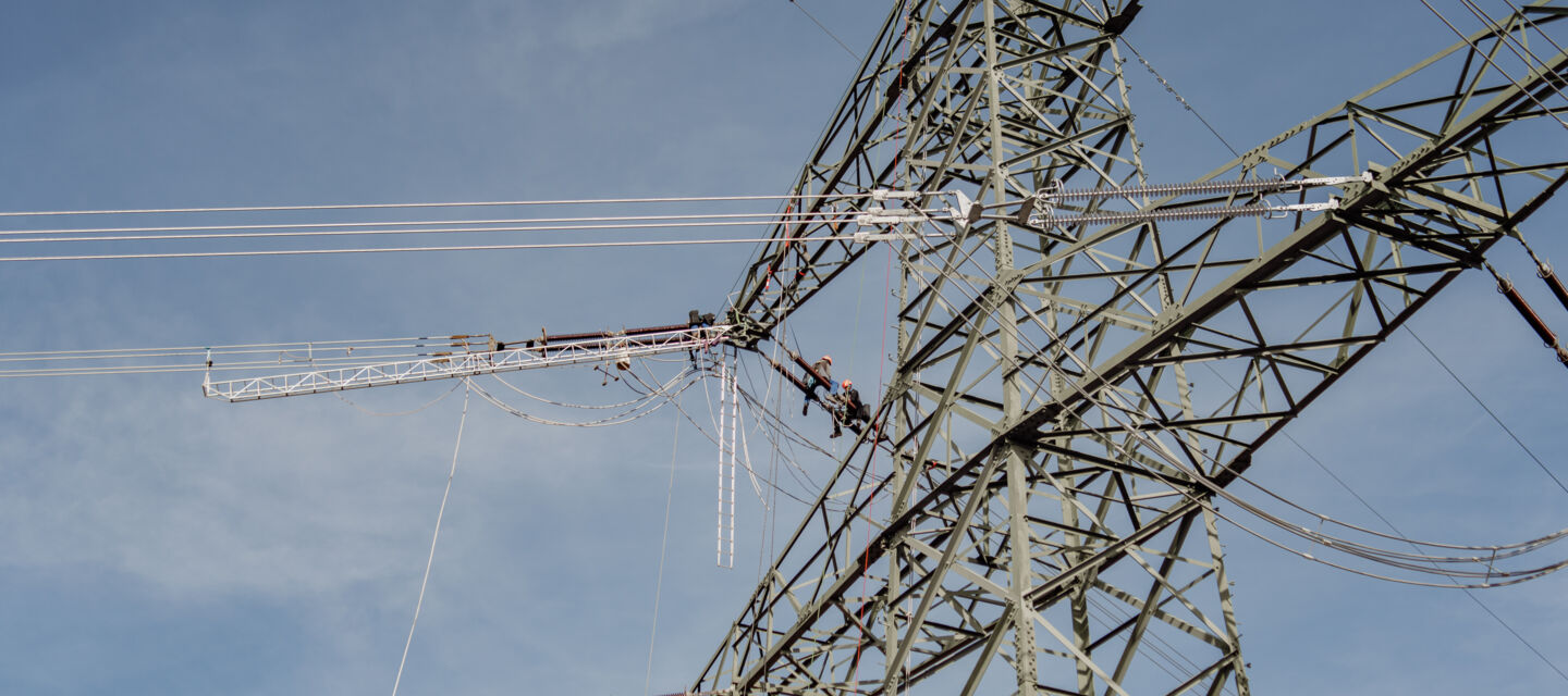 Travailleurs Cteam sous une tour &eacute;lectrique, en train d'inspecter les lignes de transmission haute tension et les &eacute;quipements.