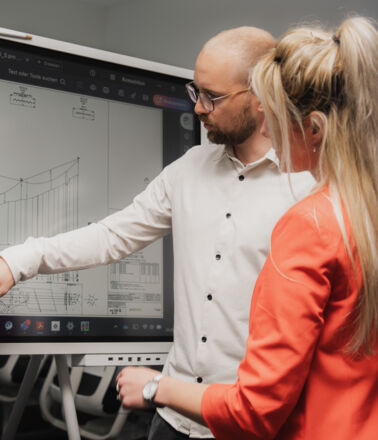 Deux collaborateurs de Cteam analysent un sch&eacute;ma technique sur un &eacute;cran interactif, partageant expertise et collaboration.