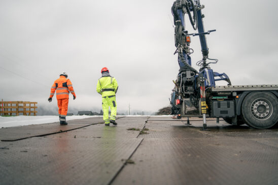 Deux travailleurs en tenue de sécurité Cteam inspectent un chantier avec grue. Deux travailleurs en tenue de sécurité Cteam inspectent un chantier avec grue.